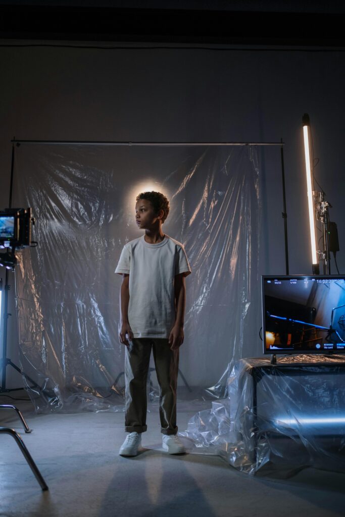A young boy stands in a contemporary studio setting with reflective surfaces and lighting.
